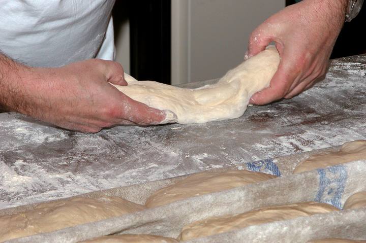 粉を振った作業台でパン生地を伸ばす両手