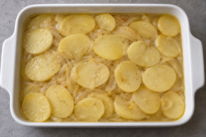 Disporre patate e cipolle a strati e versare brodo a filo